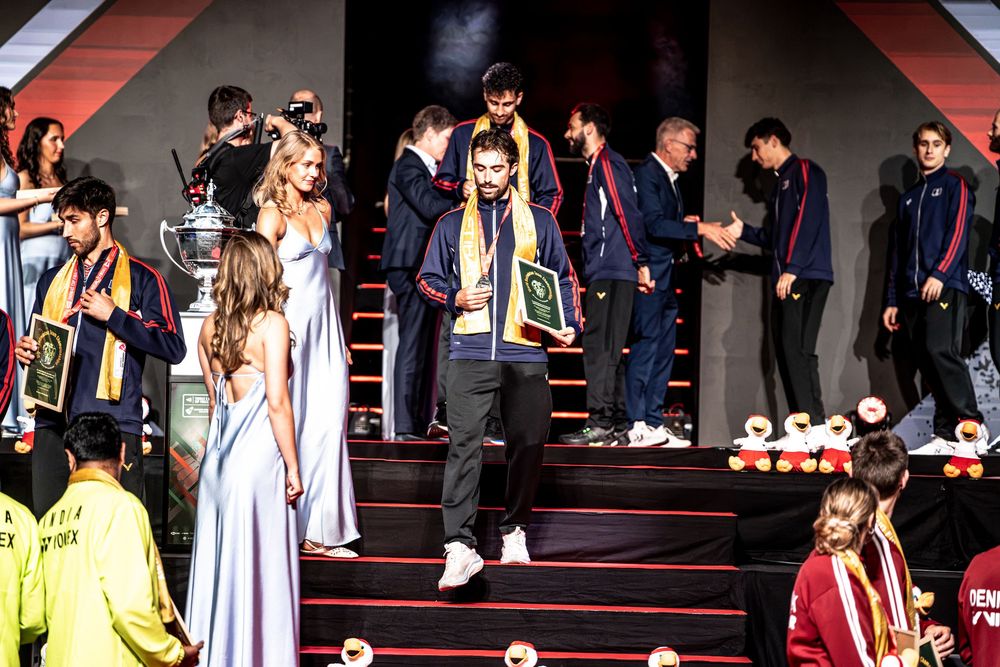 Athletes in navy uniforms descend a red-lit staircase during a sports awards ceremony with trophies.