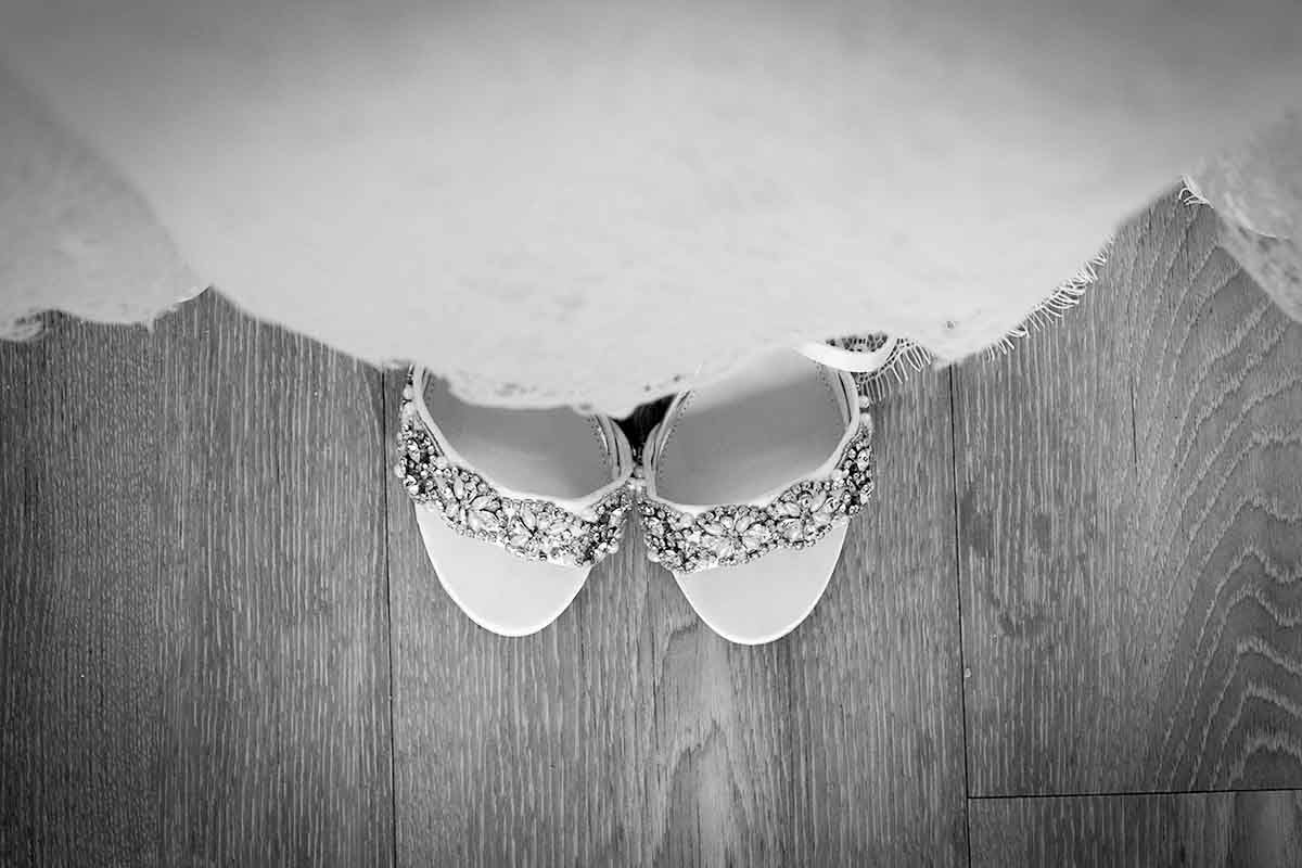 Black and white photo of elegant crystal-embellished bridal flat shoes resting on a wooden floor.
