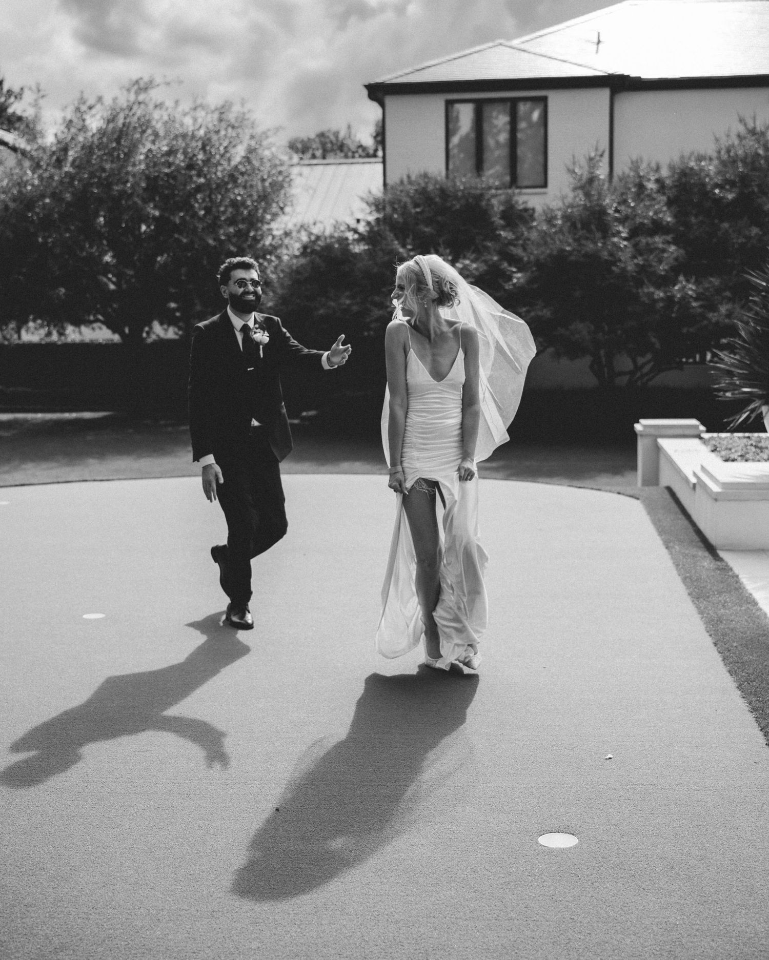 Black and white photo of a bride and groom walking outdoors on their wedding day near a house.