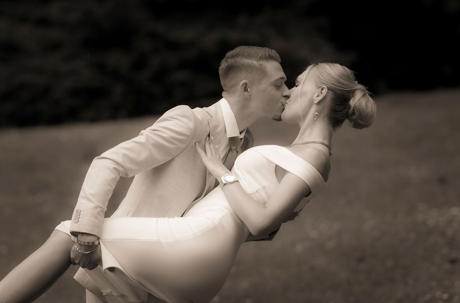 Groom dipping bride for a kiss in a classic sepia-toned outdoor wedding photo.