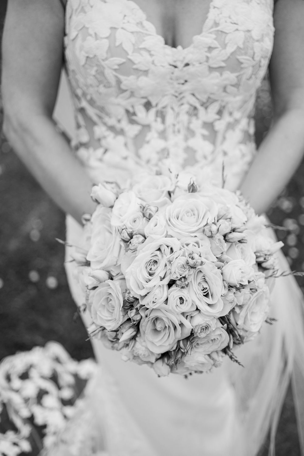 Bride holds lush round bouquet of roses and flowers in black and white wedding photo.