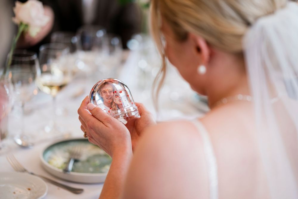 Bride examines small snow globe keepsake while seated at elegant wedding reception table.