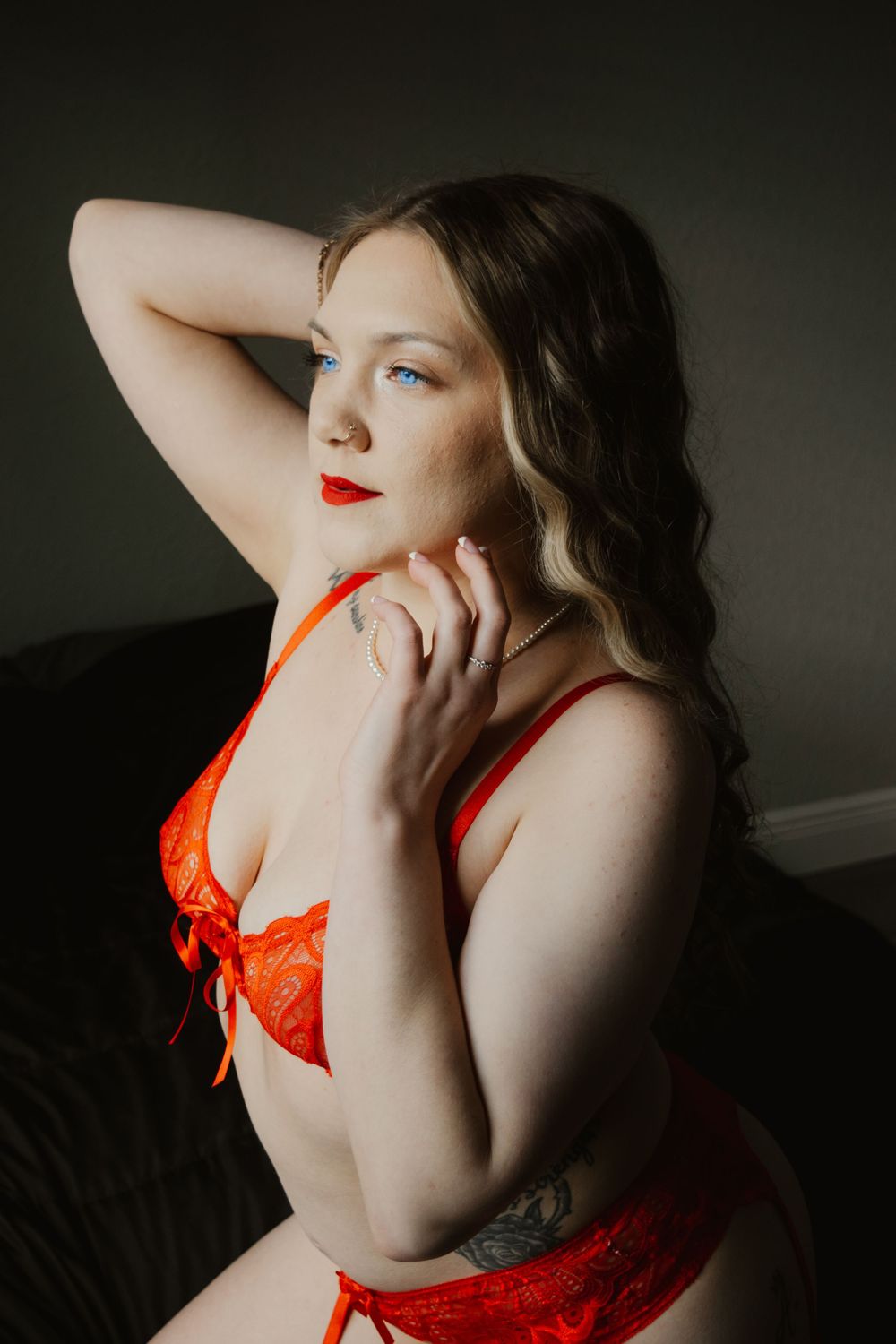 Woman with blue eyes in red lace lingerie posing in dramatic moody lighting.