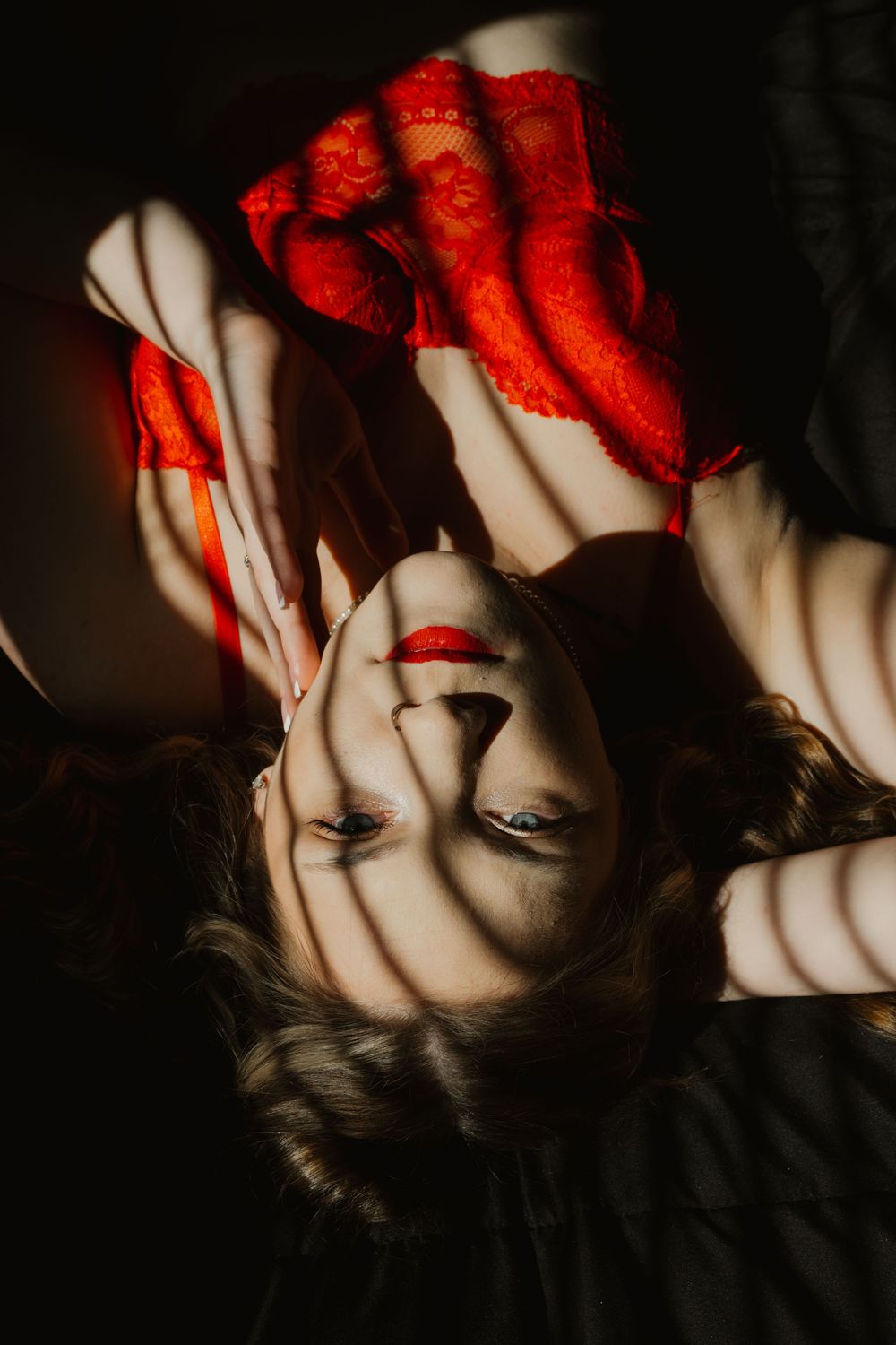 Artistic overhead shot of woman in red lingerie with dramatic shadow patterns across her face.