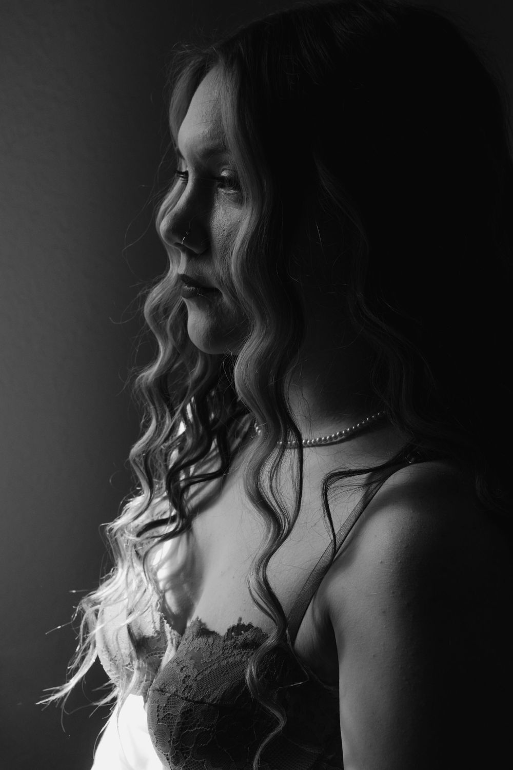 Black and white portrait of woman in lace lingerie with wavy hair in moody lighting.