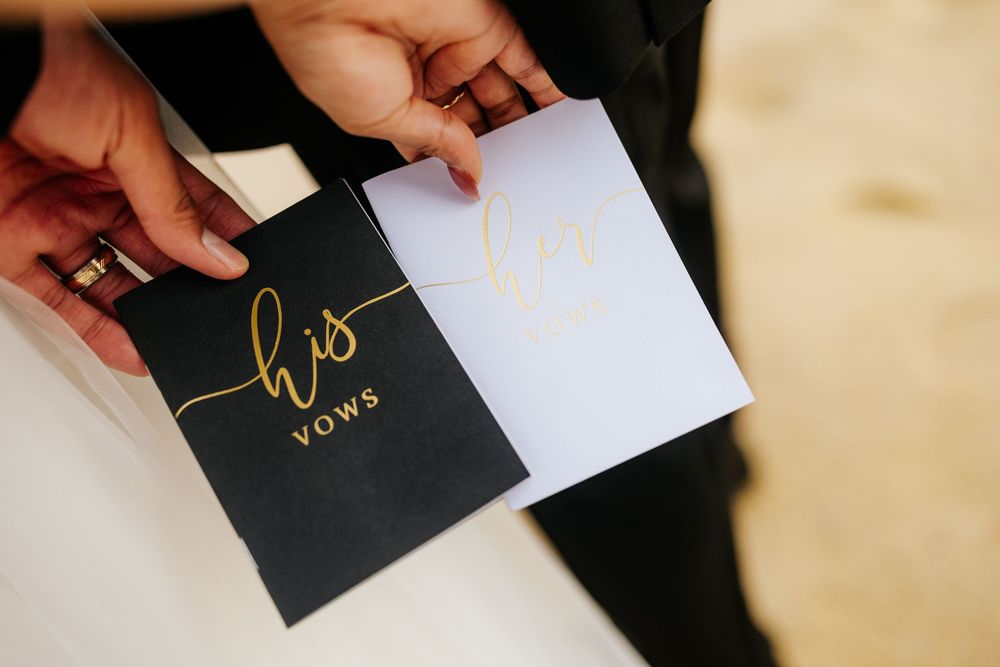 Close-up of elegant black and white wedding vow booklets with gold script lettering held by a couple.
