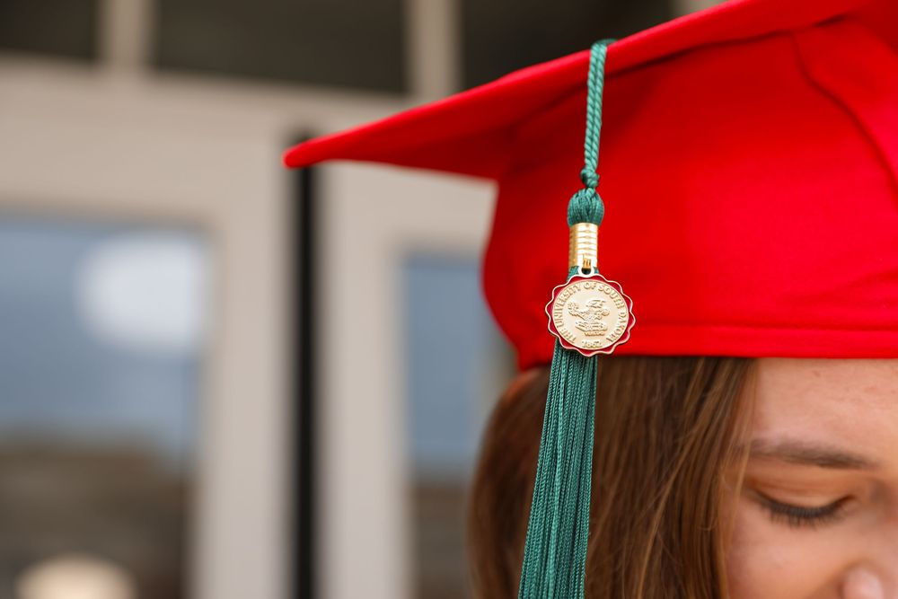Close-up of a red graduation cap with a green tassel and gold medallion worn by a female graduate.