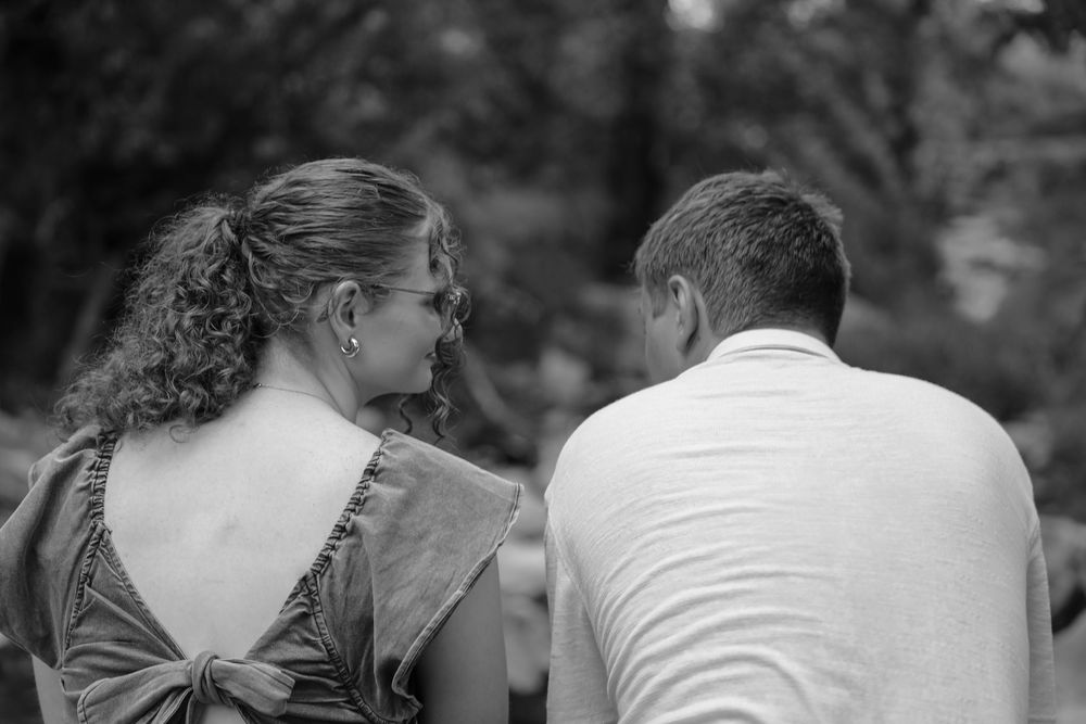 Black and white photo of a couple seen from behind, woman in backless bow dress, man in white shirt outdoors.