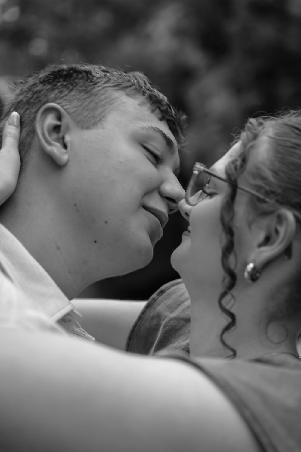 Black and white photo of a young couple sharing a romantic nose-to-nose moment, woman wearing glasses.