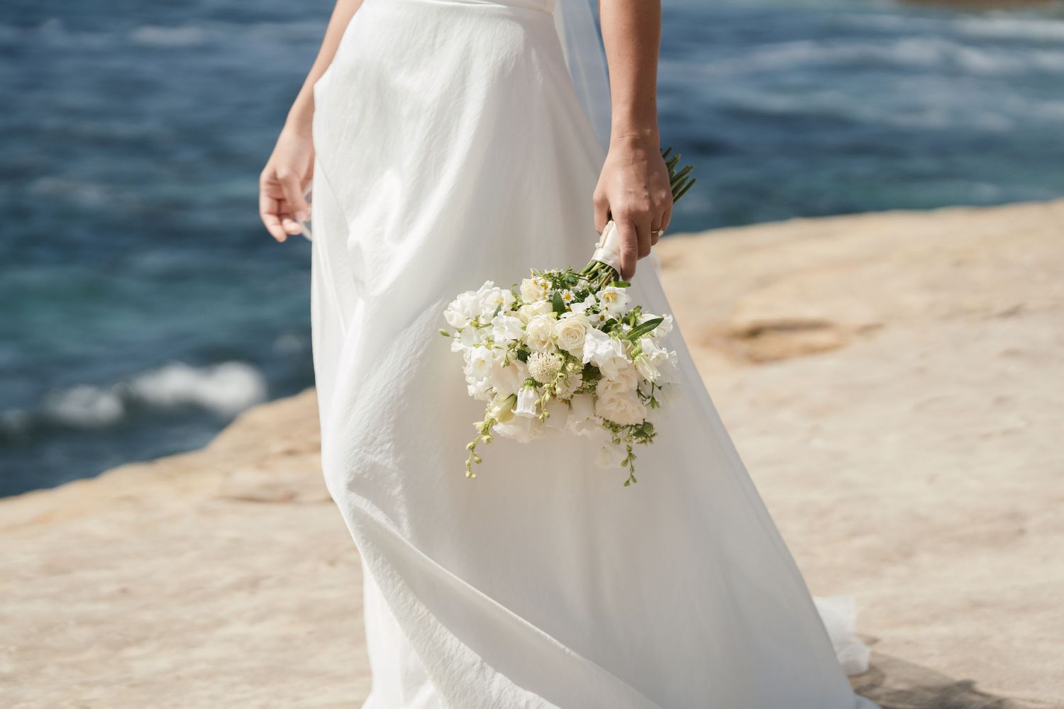 A bride holds her bouquet beside her at the beach in La Jolla.