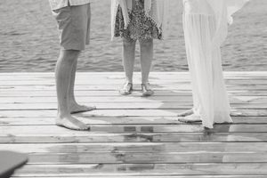 Black and white photo of barefoot adults and child standing on a wooden dock by the water.