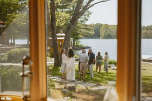 Group of people walking toward a serene lakeside setting on a sunny day, viewed through a wooden window frame.