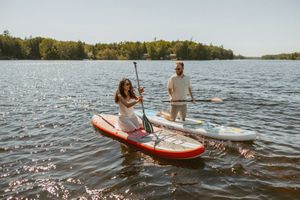 Couple paddleboarding on a calm lake surrounded by lush green trees on a sunny day.
