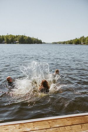 Person diving into a calm lake from a wooden dock, creating a large splash on a sunny summer day.