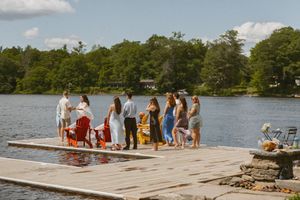Group of guests gathering on a lakeside dock surrounded by lush trees on a sunny summer day.