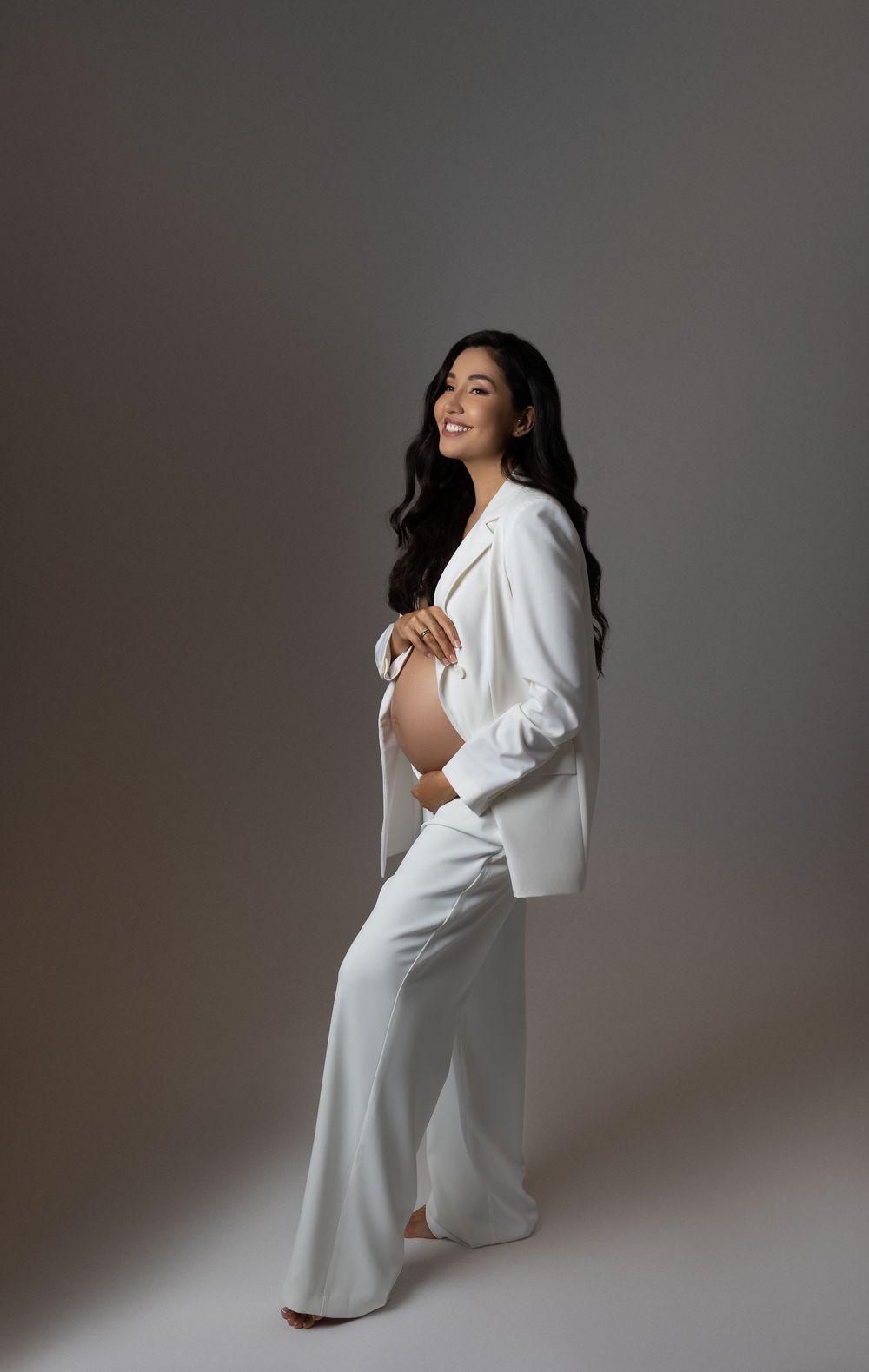 An artistic maternity photo series shows a person in a flowing white dress against a grey studio background.