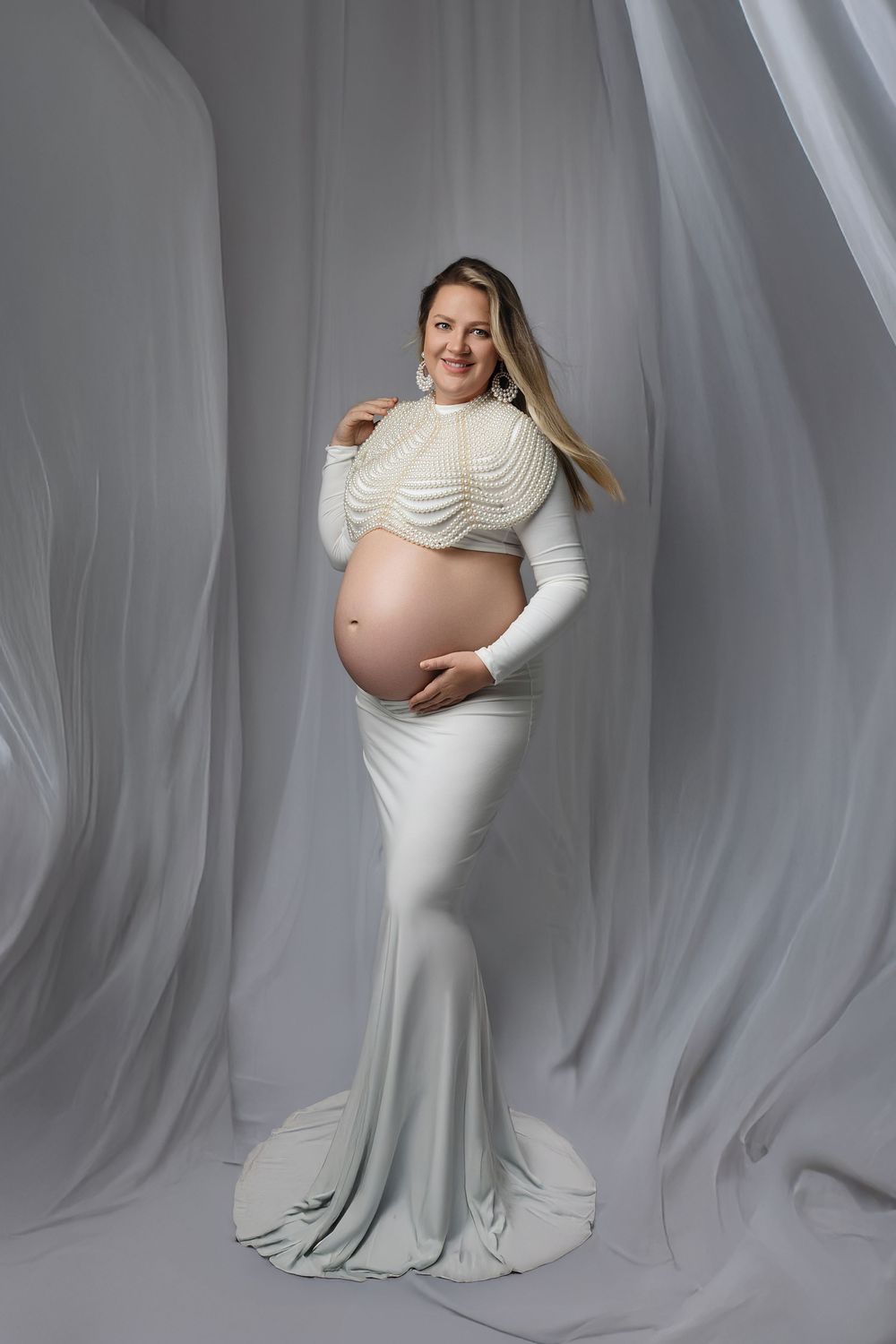 A maternity photoshoot series showing poses in a white fitted dress against a light gray backdrop.