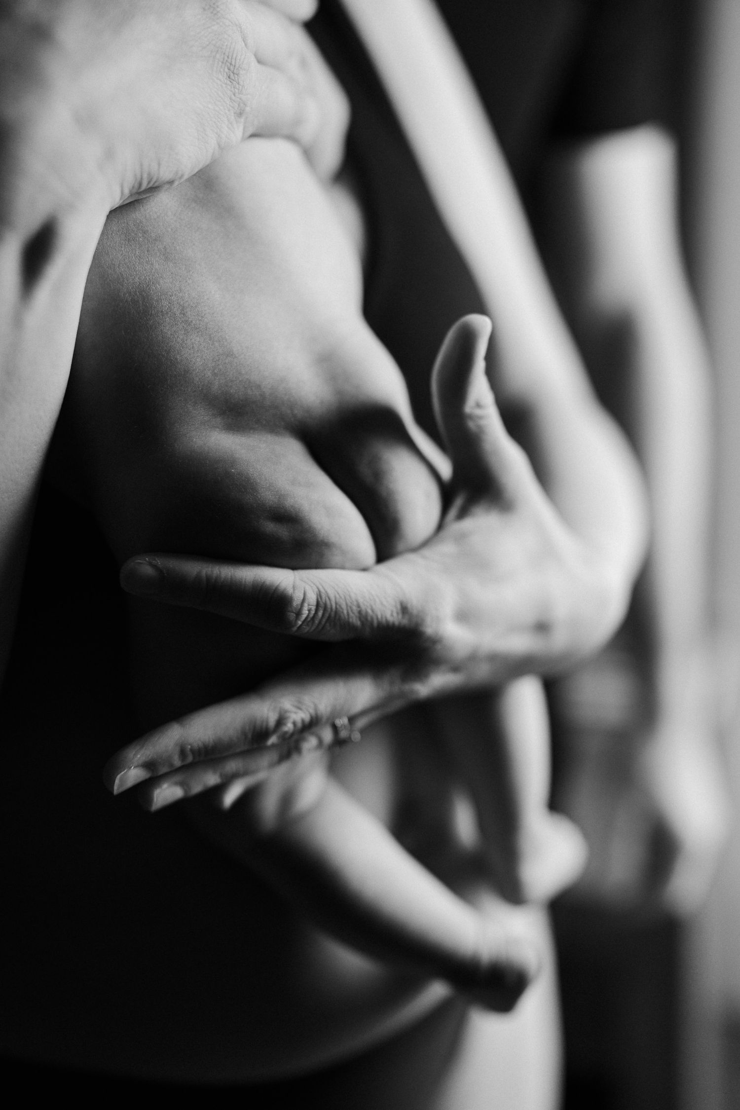 Black and white close-up of intertwined hands and torso, showcasing human form and connection.
