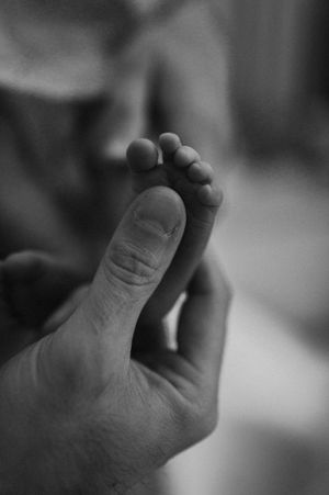 Black and white photo of an adult hand gently holding a newborn baby's tiny foot, symbolizing love and new life.