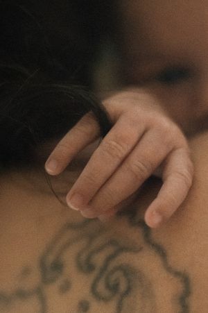 A hand holding a glass resting on tattooed skin with ornate dark ink designs, moody and artistic photography.