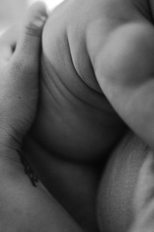 Close-up black and white photo of a newborn baby's tiny feet cradled gently in an adult's hand.