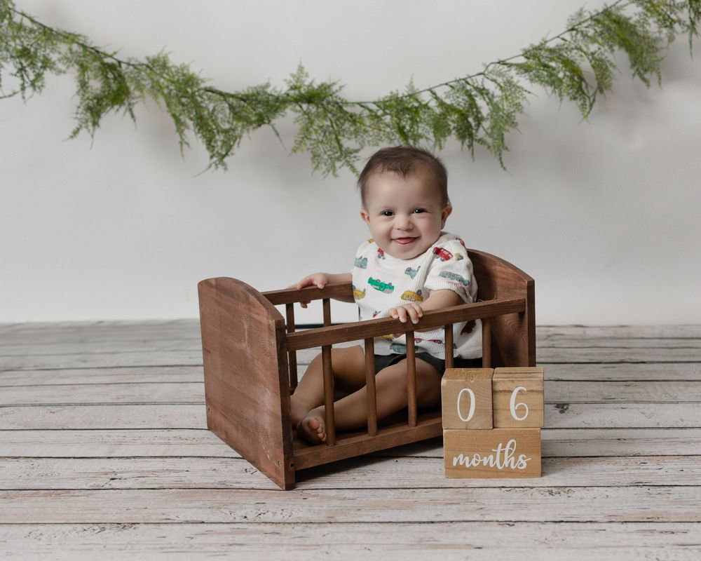 Rustic wooden baby bed photographed in sequence with evergreen garland and wood sign decorations against white backdrop.