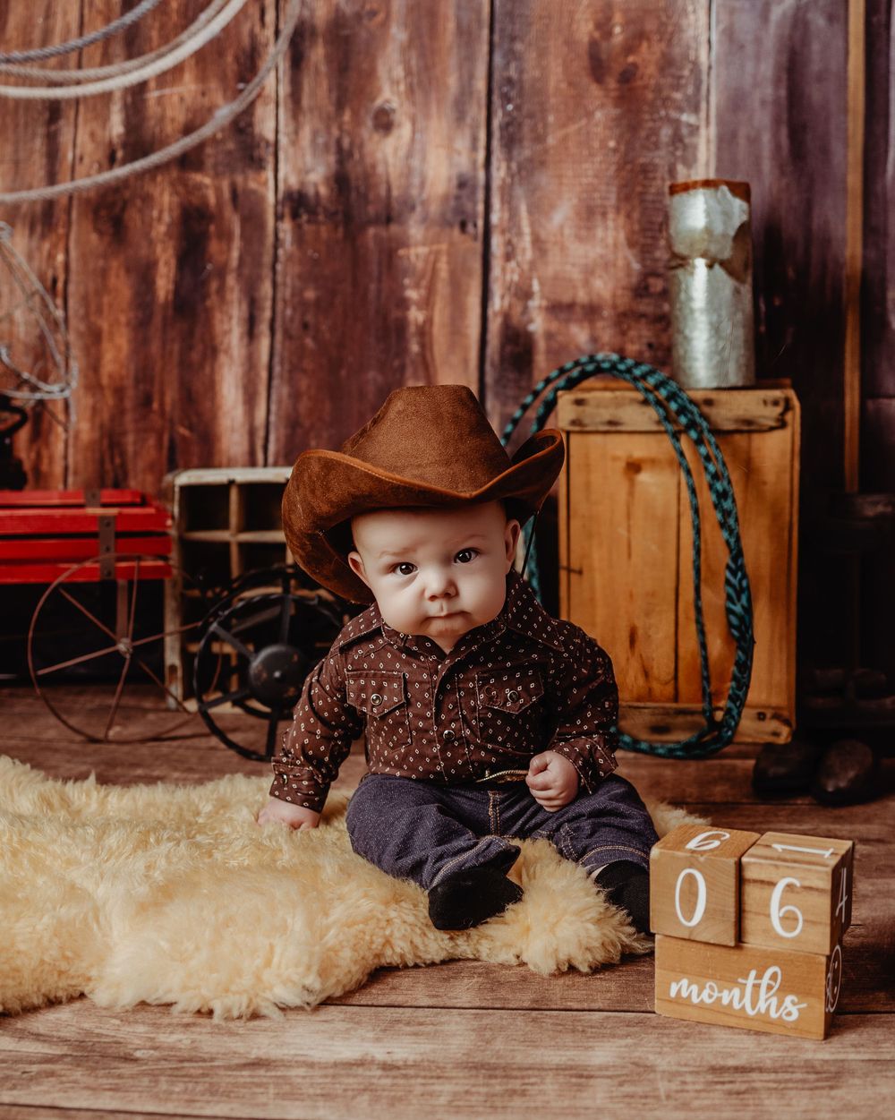 Four rustic styled photos featuring a baby in country western attire sitting on a sheepskin rug in a wooden barn setting.