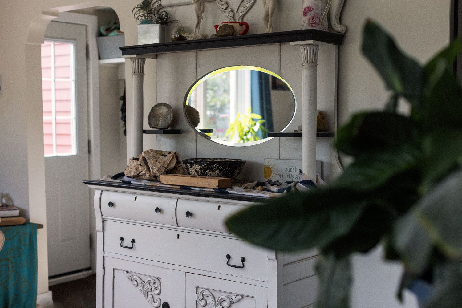 Vintage white dresser with ornate carvings, oval mirror, and decorative items on top in a cozy room.