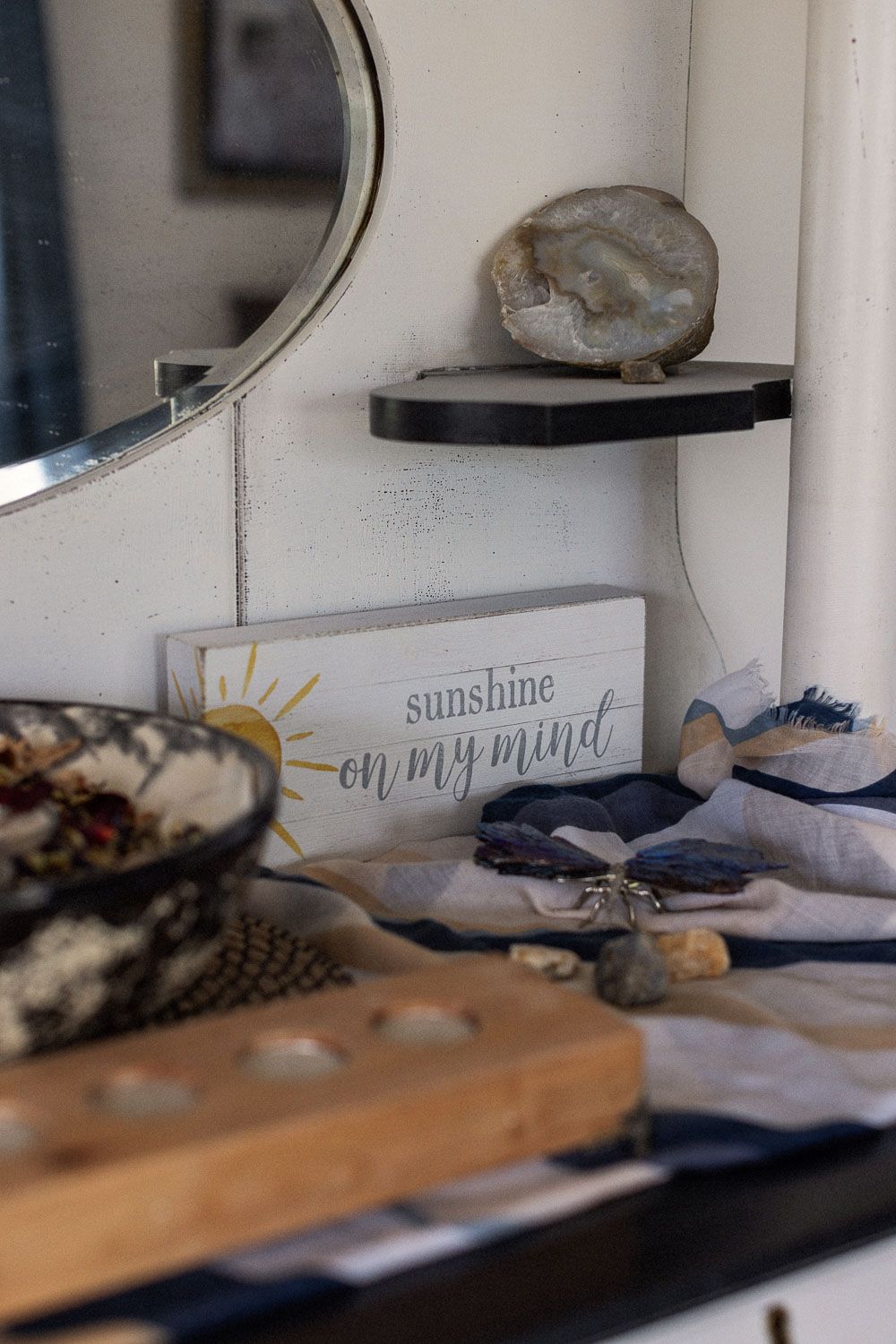 Cozy shelf decor with a sunshine sign, geode crystal, mirror, and linen fabric in a rustic home setting.