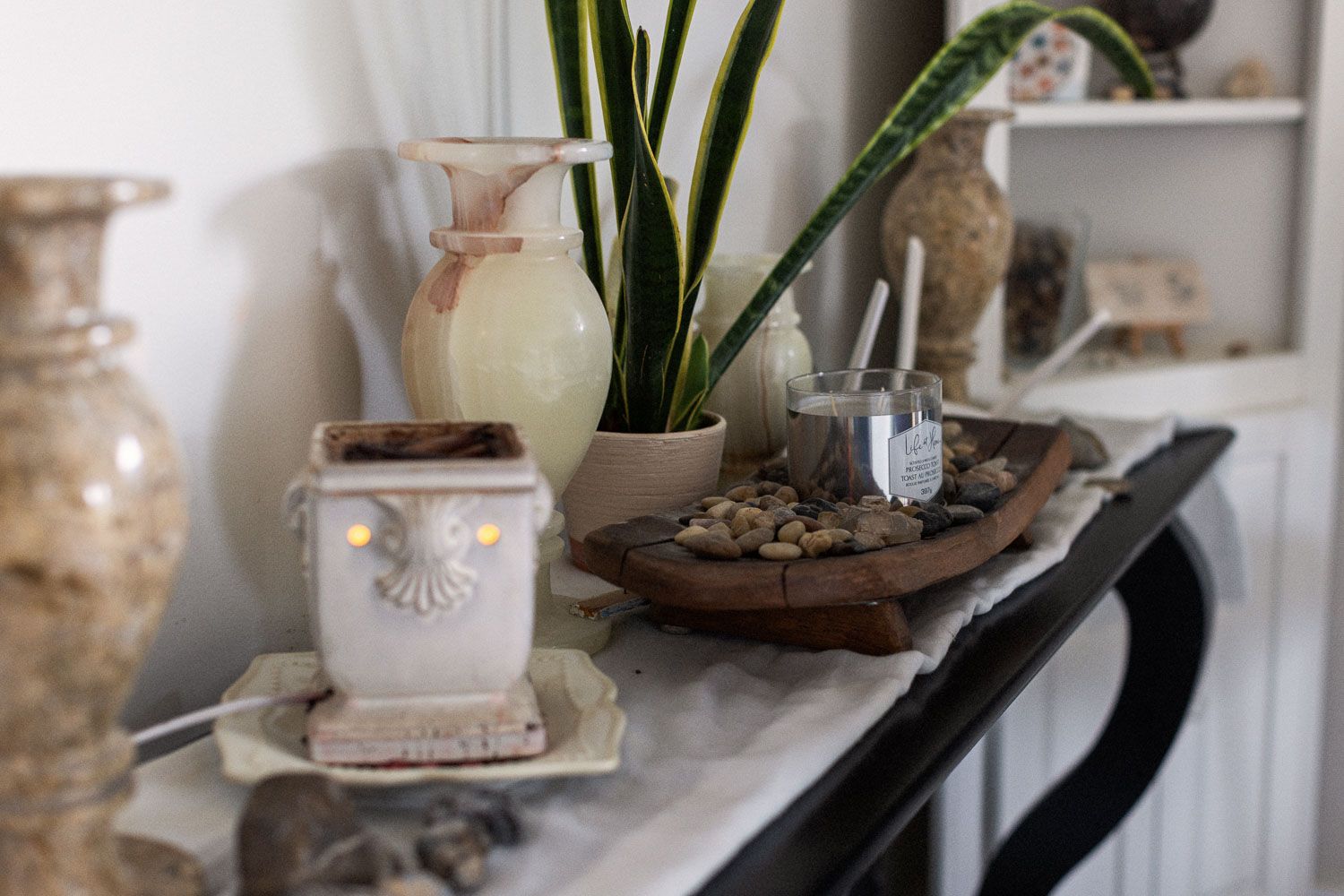 Decorative mantel display with white ceramic wax warmer, snake plant, stone tray, and rustic vases.