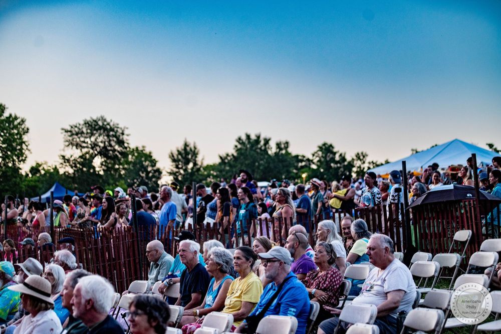Large crowd of people seated and standing at an outdoor music festival during golden hour.