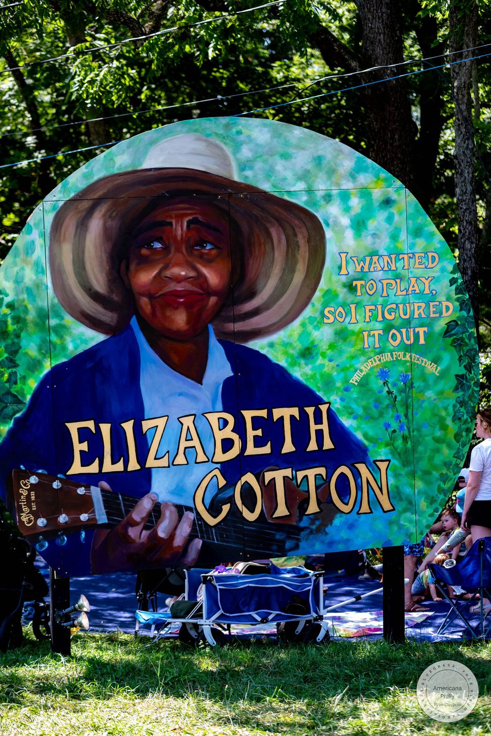 Colorful outdoor mural of blues musician Elizabeth Cotton playing guitar with inspirational quote at a music festival.