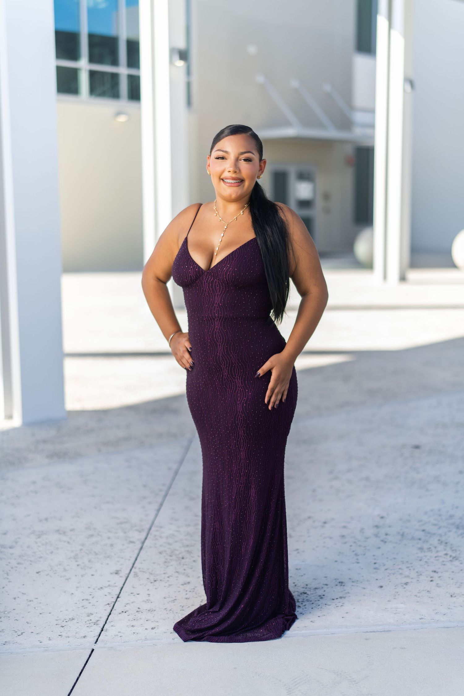 Woman in elegant purple glitter gown posing outdoors at formal event, smiling confidently.