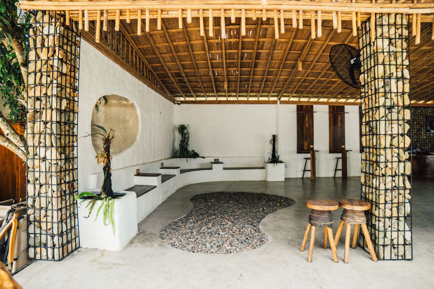 Rustic bamboo hut with thatched palm leaf roof surrounded by lush tropical greenery and coconut trees.