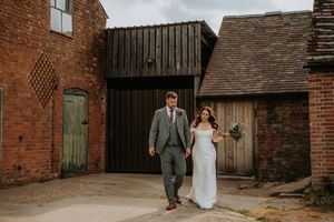 Bride and groom walking hand in hand outside a rustic brick barn venue on their wedding day.