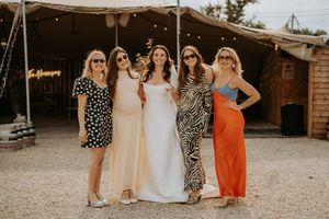 Bride in white gown poses with four friends in colorful dresses outside a rustic wedding venue.