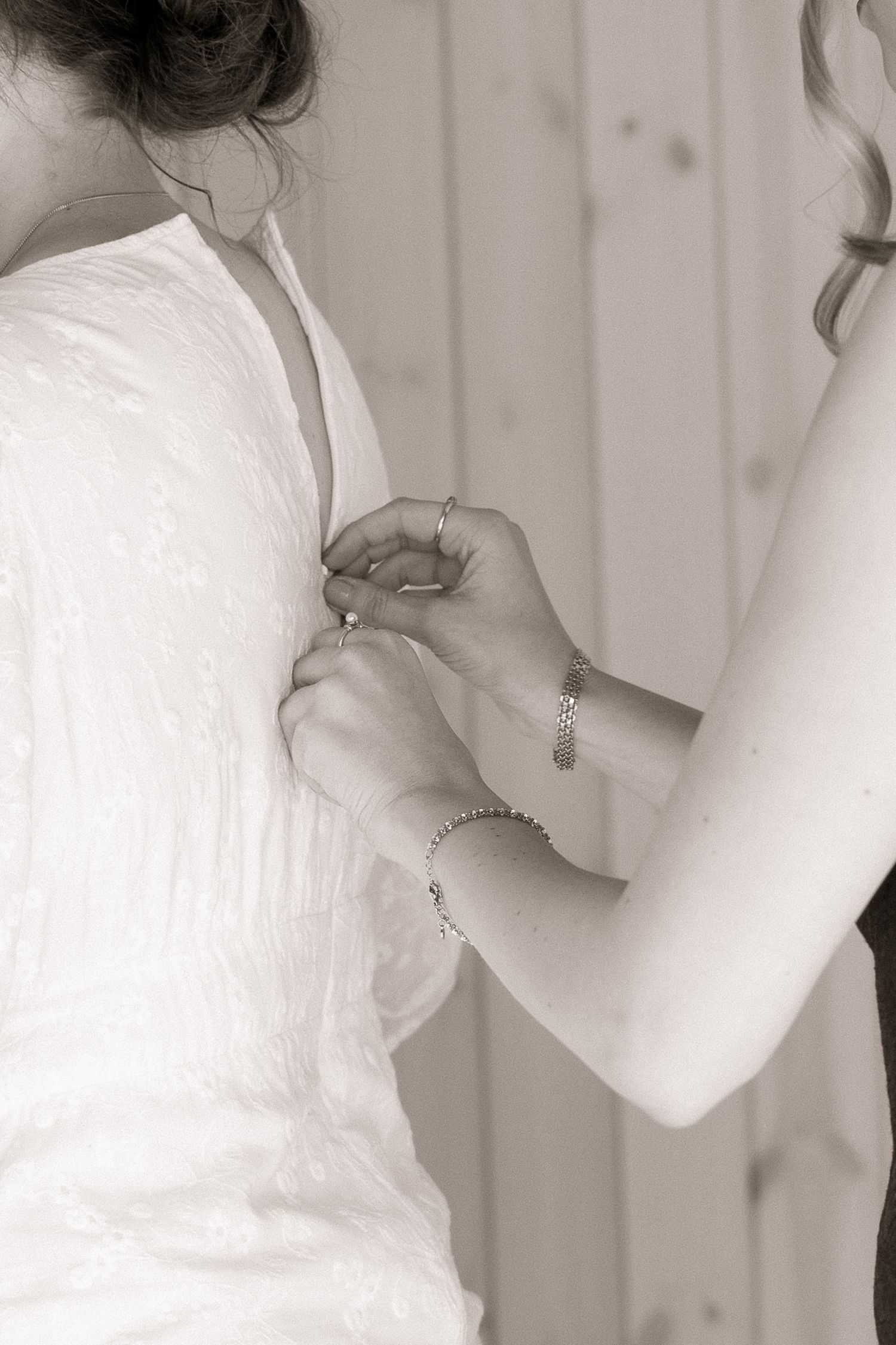 Black and white photo of a woman helping button the back of a white wedding dress.