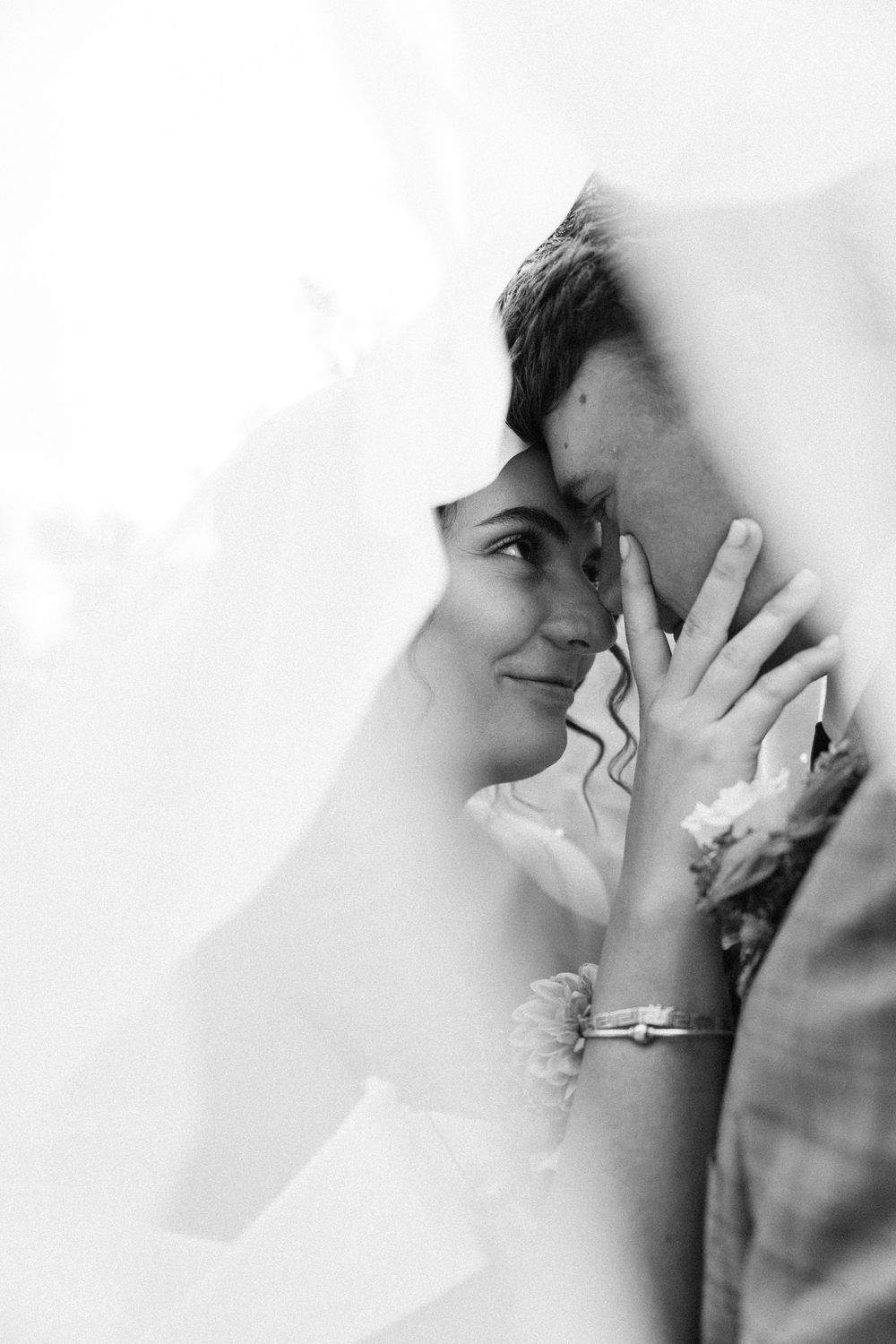Black and white photo of bride and groom sharing intimate moment under wedding veil.