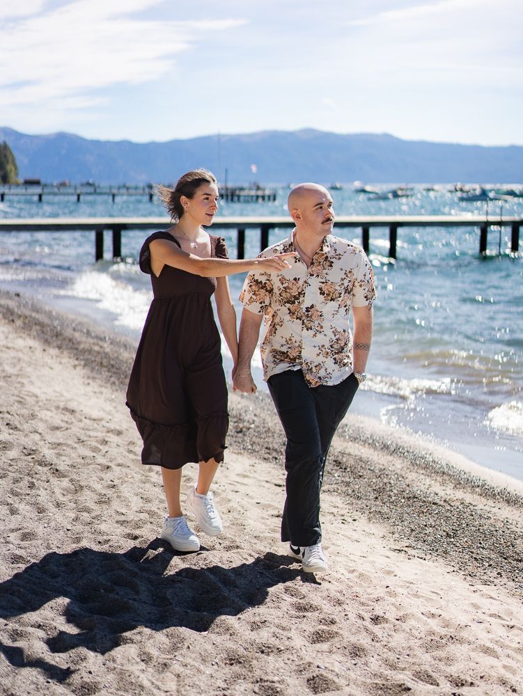 Couple walking hand-in-hand on a sandy Lake Tahoe beach, woman in brown dress, man in floral shirt.