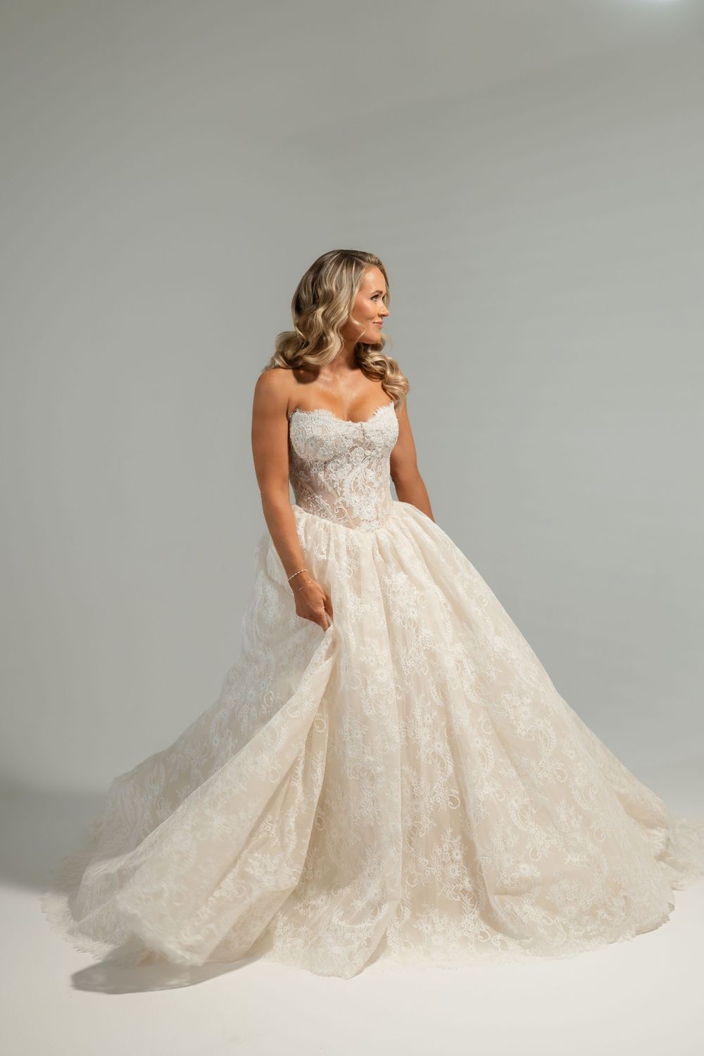 Bride in strapless lace ballgown wedding dress with sweetheart neckline and full skirt posing in studio.