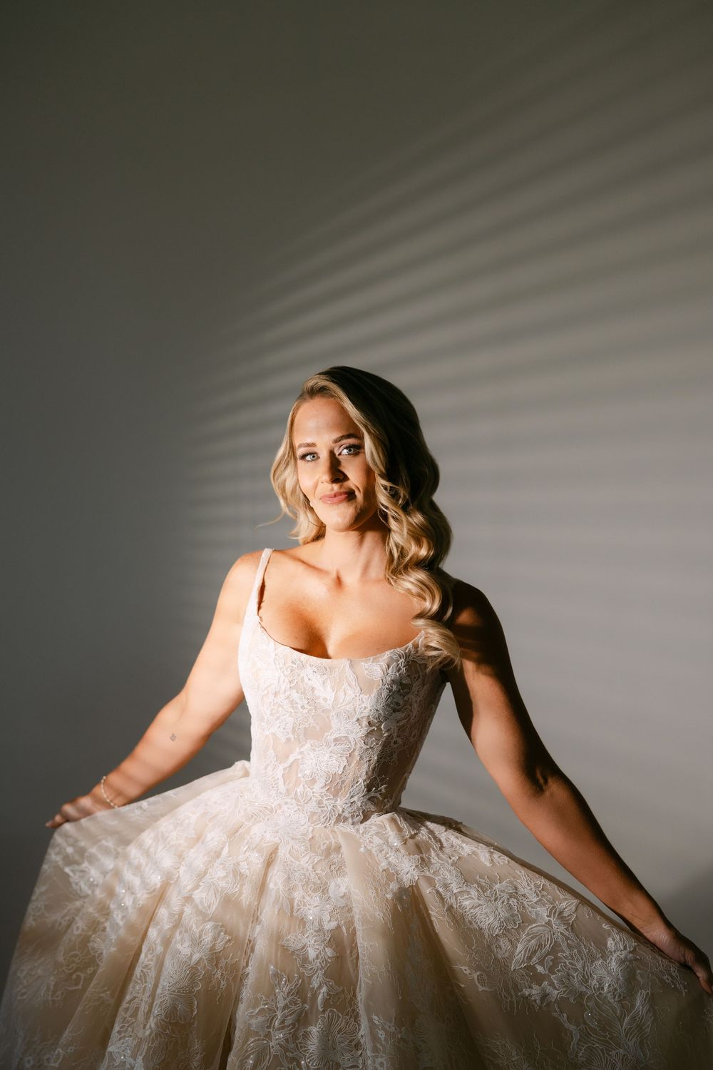 Blonde bride in lace ballgown posing gracefully in dramatic light.