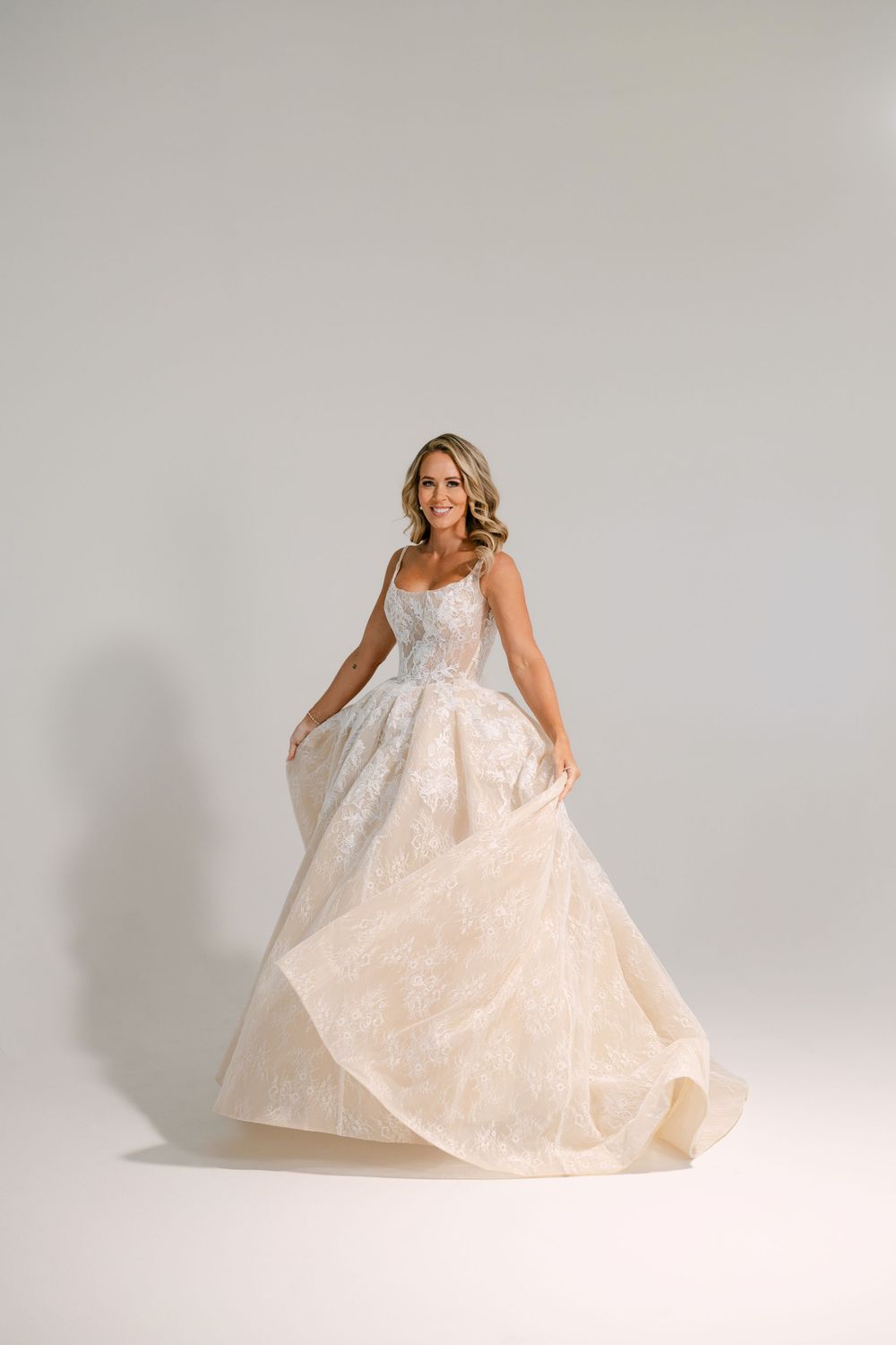 Bride twirling in a champagne floral ballgown with lace bodice and full skirt in a bright studio.