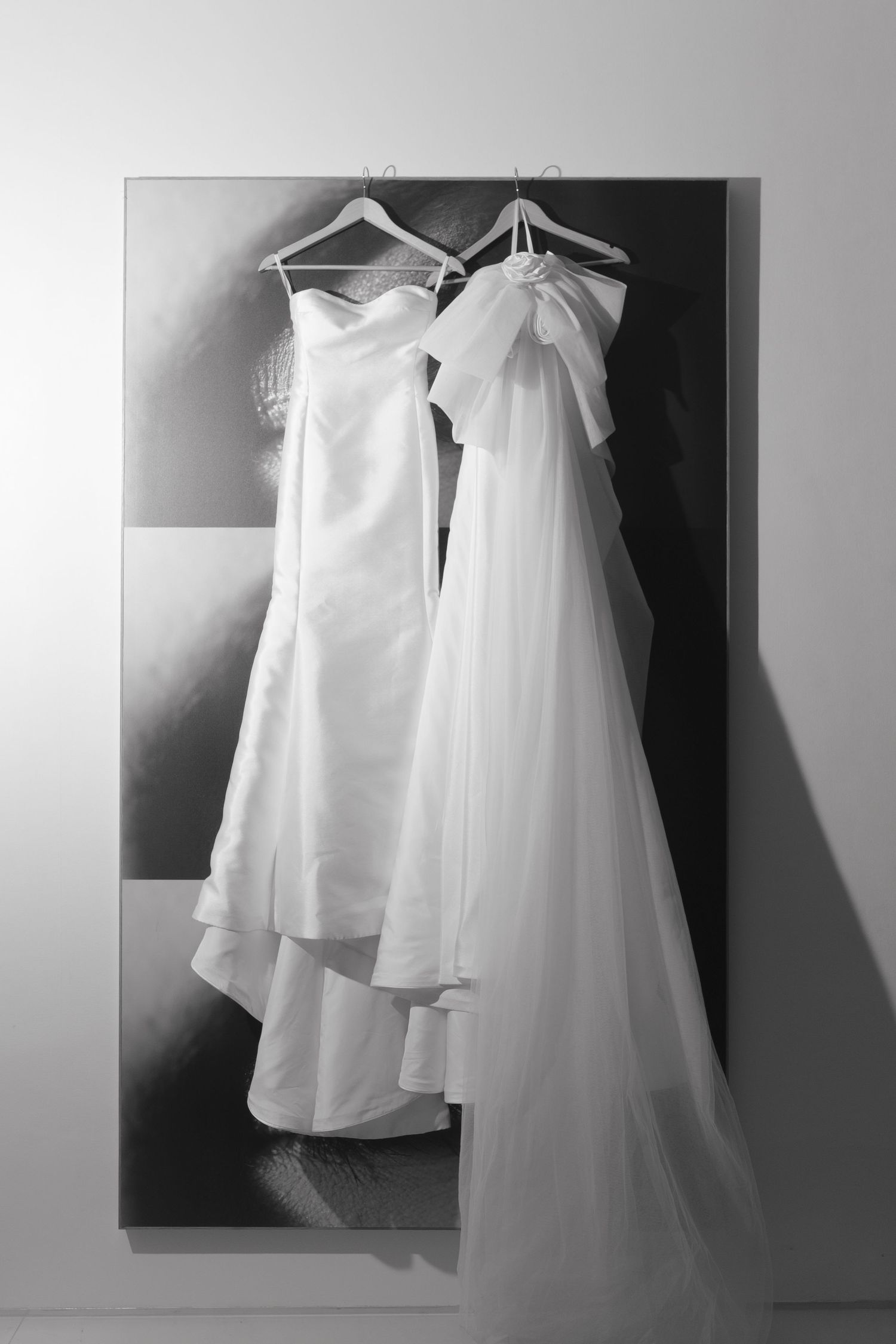Elegant white wedding dress and veil hanging on hangers against a modern art canvas.