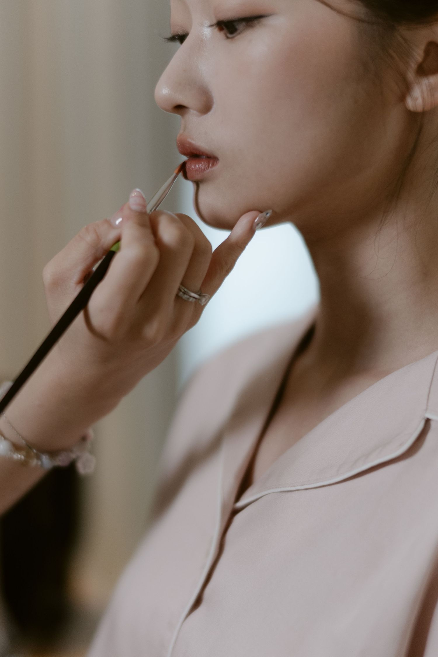 Close-up of a makeup artist applying lipstick to an Asian bride during bridal preparation.