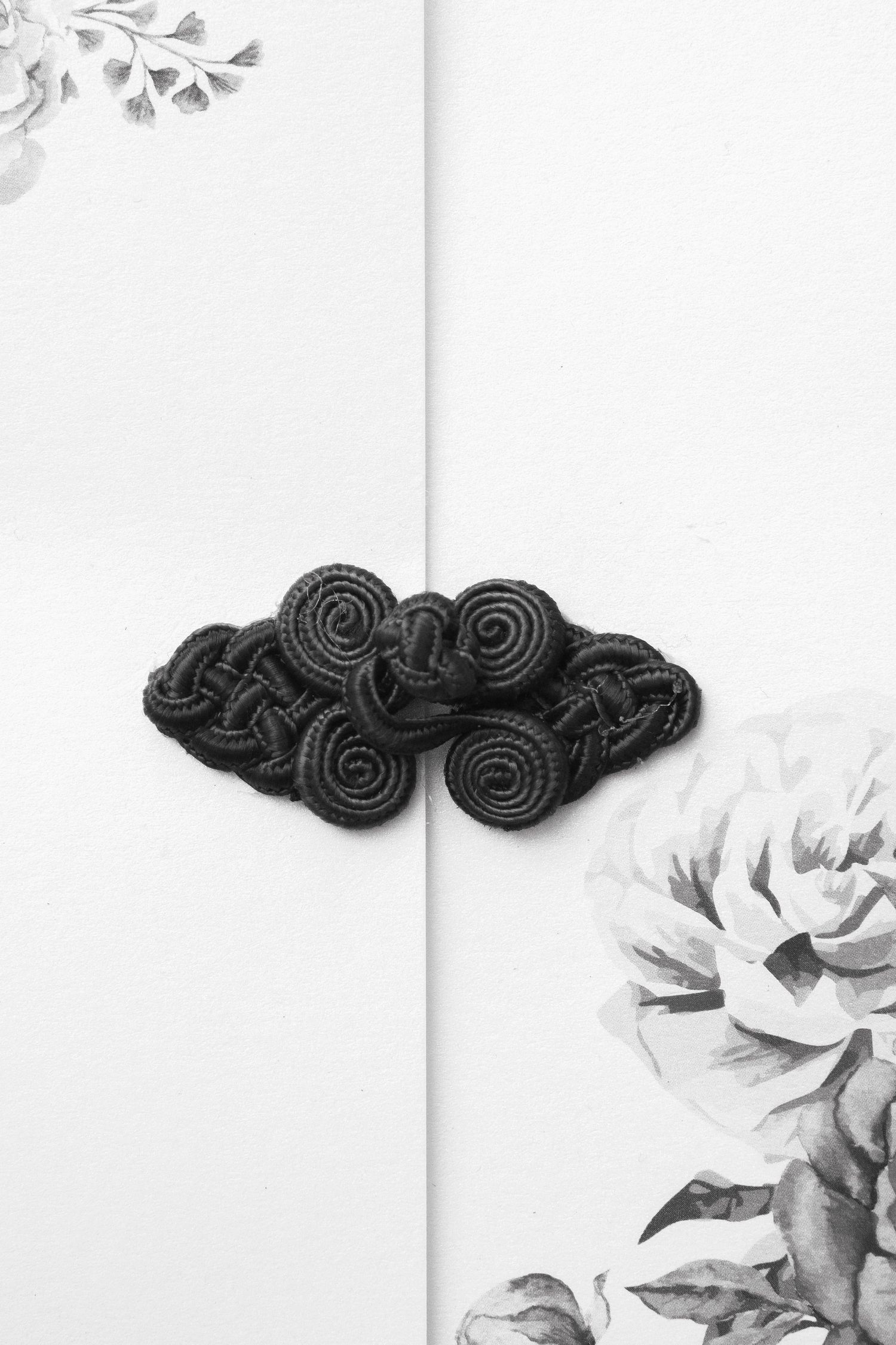 Black decorative Chinese frog closure button on white floral background in elegant black and white photography.