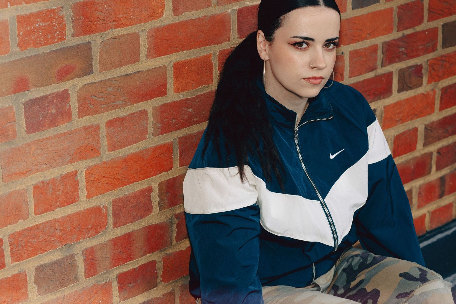 Young woman in a navy blue and white Nike windbreaker jacket posing outdoors in an urban setting.