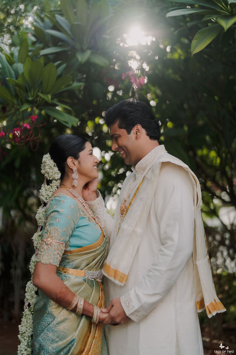 South Indian bride and groom in traditional wedding attire share a joyful moment among tropical greenery.