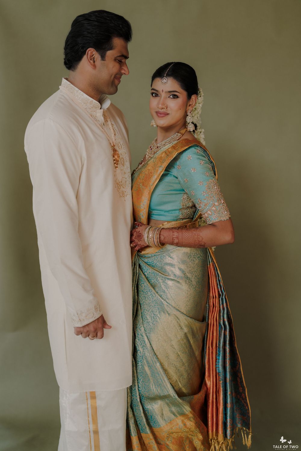 South Indian couple in traditional wedding attire, groom in cream kurta, bride in teal and gold Kanjivaram saree.
