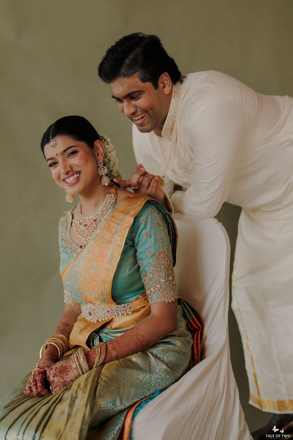 Groom adjusting brides teal and gold Kanjivaram saree necklace during South Indian wedding ceremony.