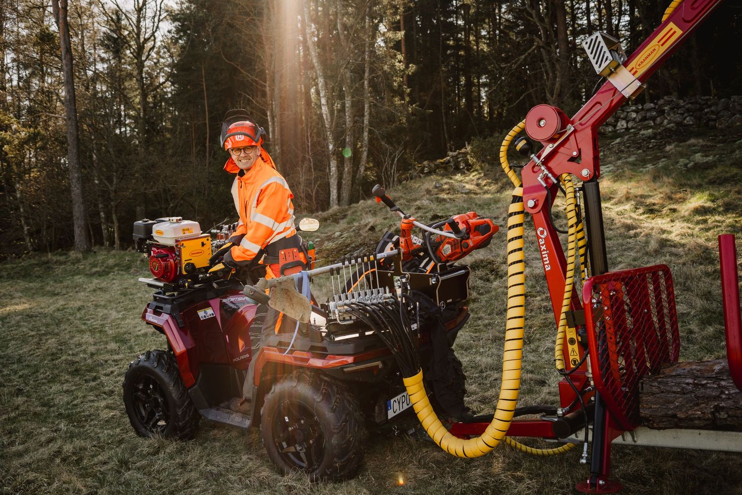 Worker in orange safety gear operating a red ATV with forestry equipment attachment in a woodland setting.